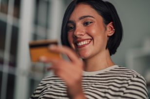 Jeune femme aux cheveux courts et foncés, souriant joyeusement en tenant une carte bancaire dorée.