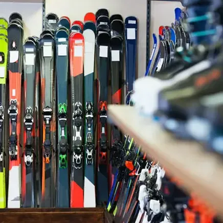 De nombreux skis colorés alignés dans un magasin de sport, avec des chaussures de ski floues au premier plan.