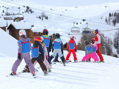 Enfants apprenant à skier avec un moniteur sur une piste enneigée, des télésièges et chalets en arrière-plan.
