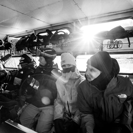 En noir et blanc, des personnes en tenue de ski dans un véhicule, le soleil éclatant à travers une fenêtre.